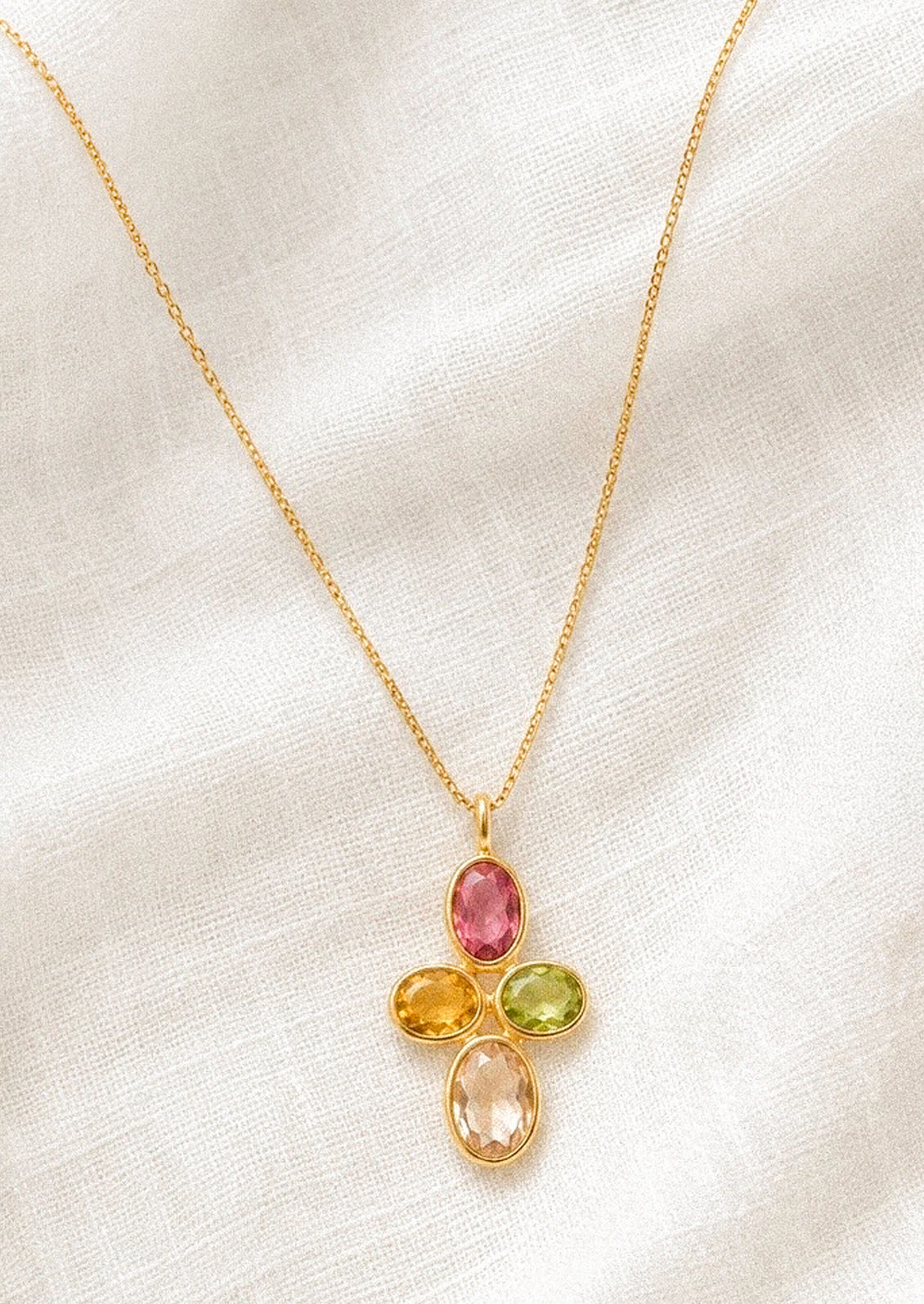 A gold chain necklace with a pendant made with colorful gems in a cross shape.