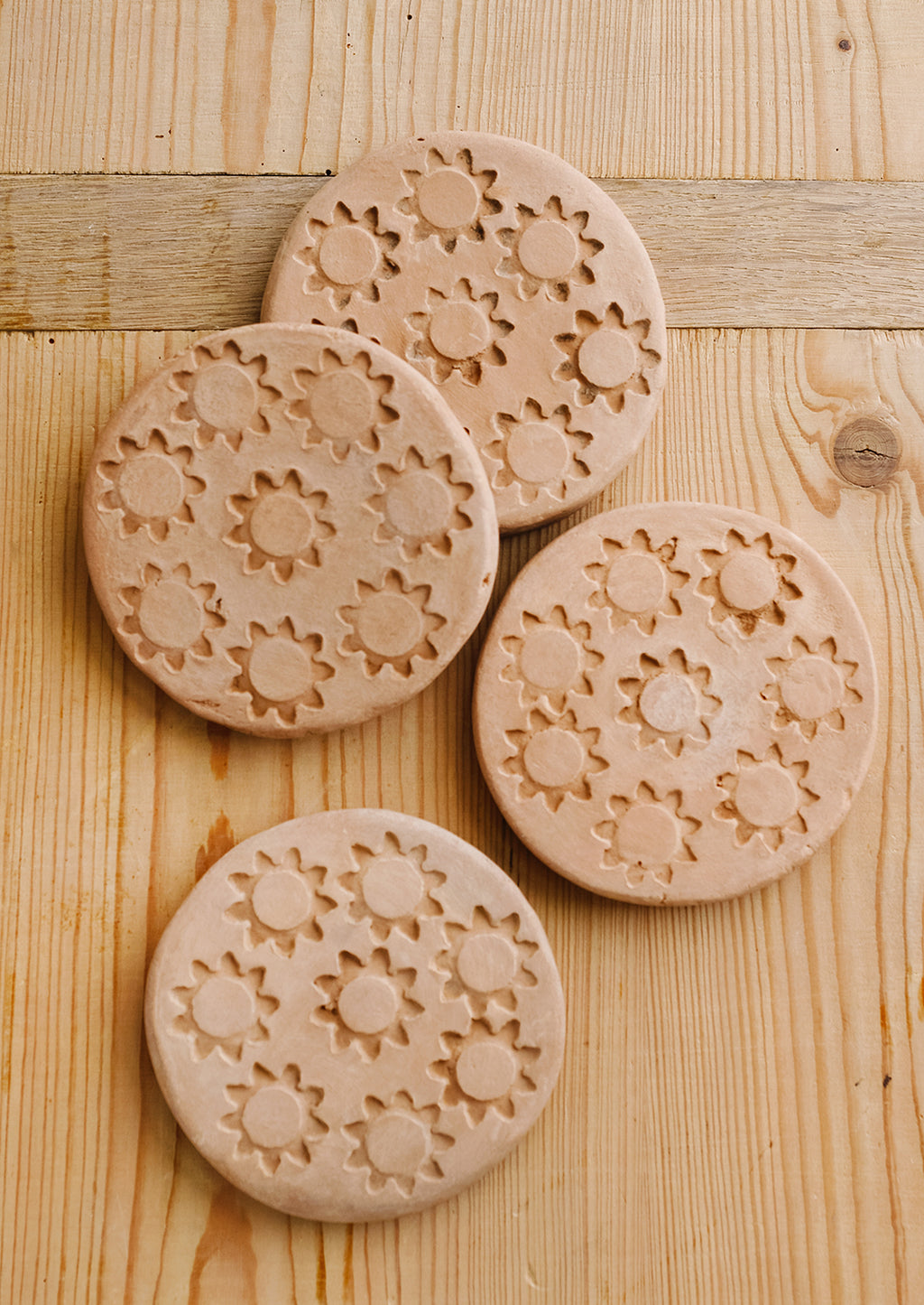 1: A set of round terracotta coasters with stamped sun pattern.