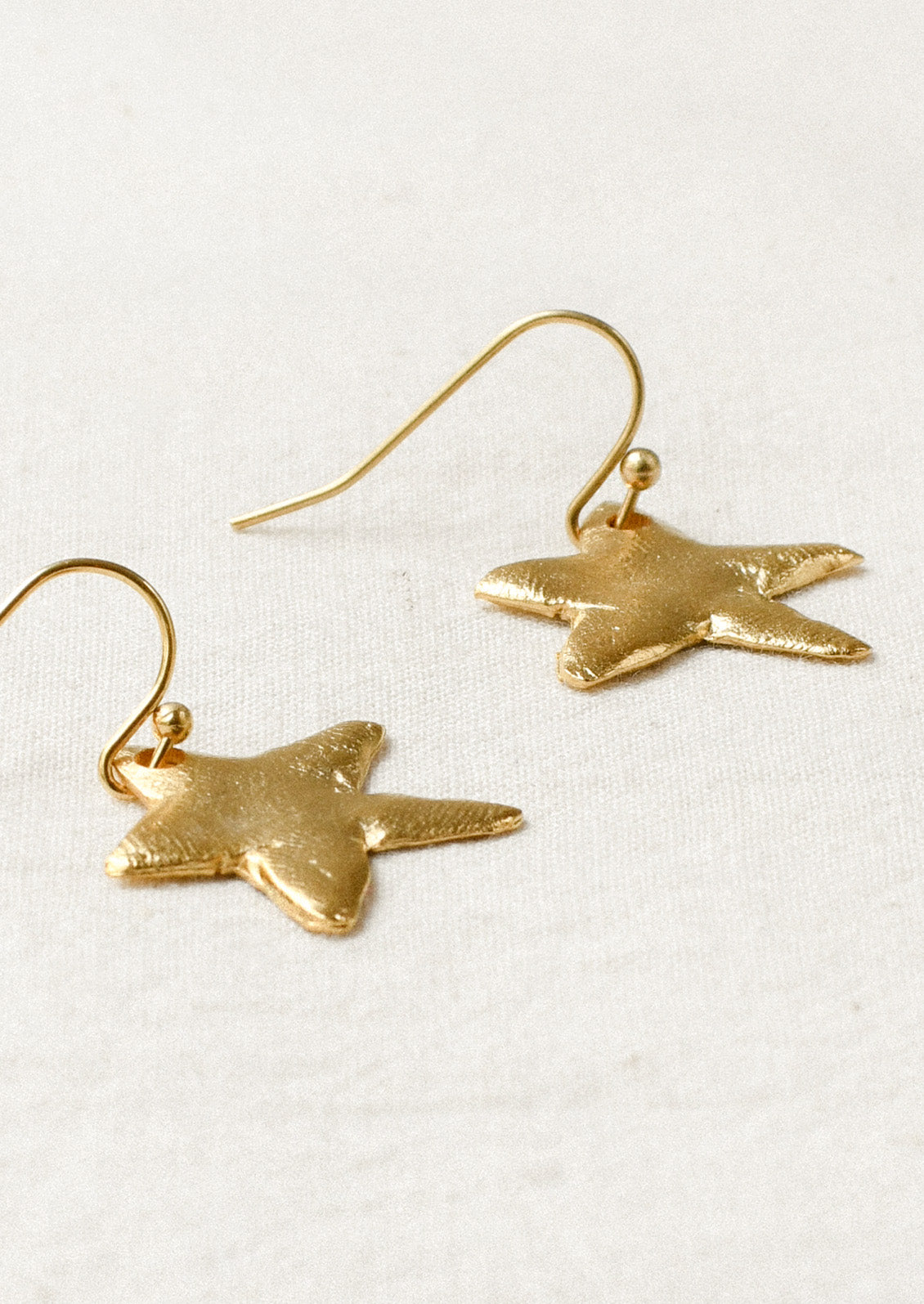 A pair of gold earrings with large dangling star shaped charms.