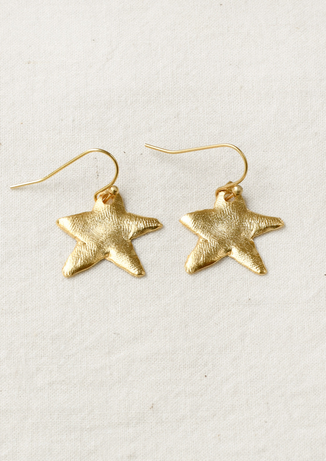 A pair of gold earrings with large dangling star shaped charms.