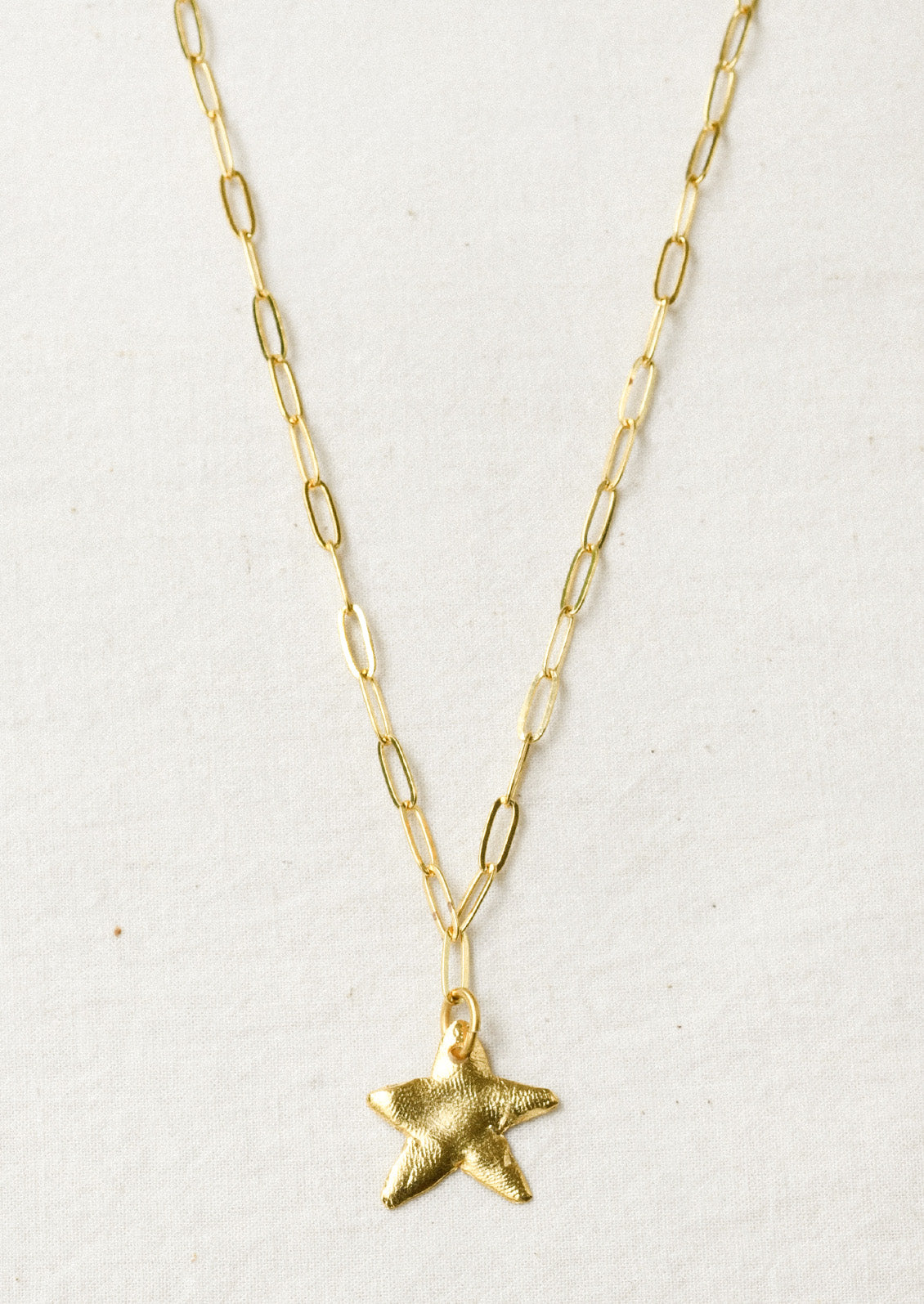 A gold paperclip chain necklace with a large star pendant.