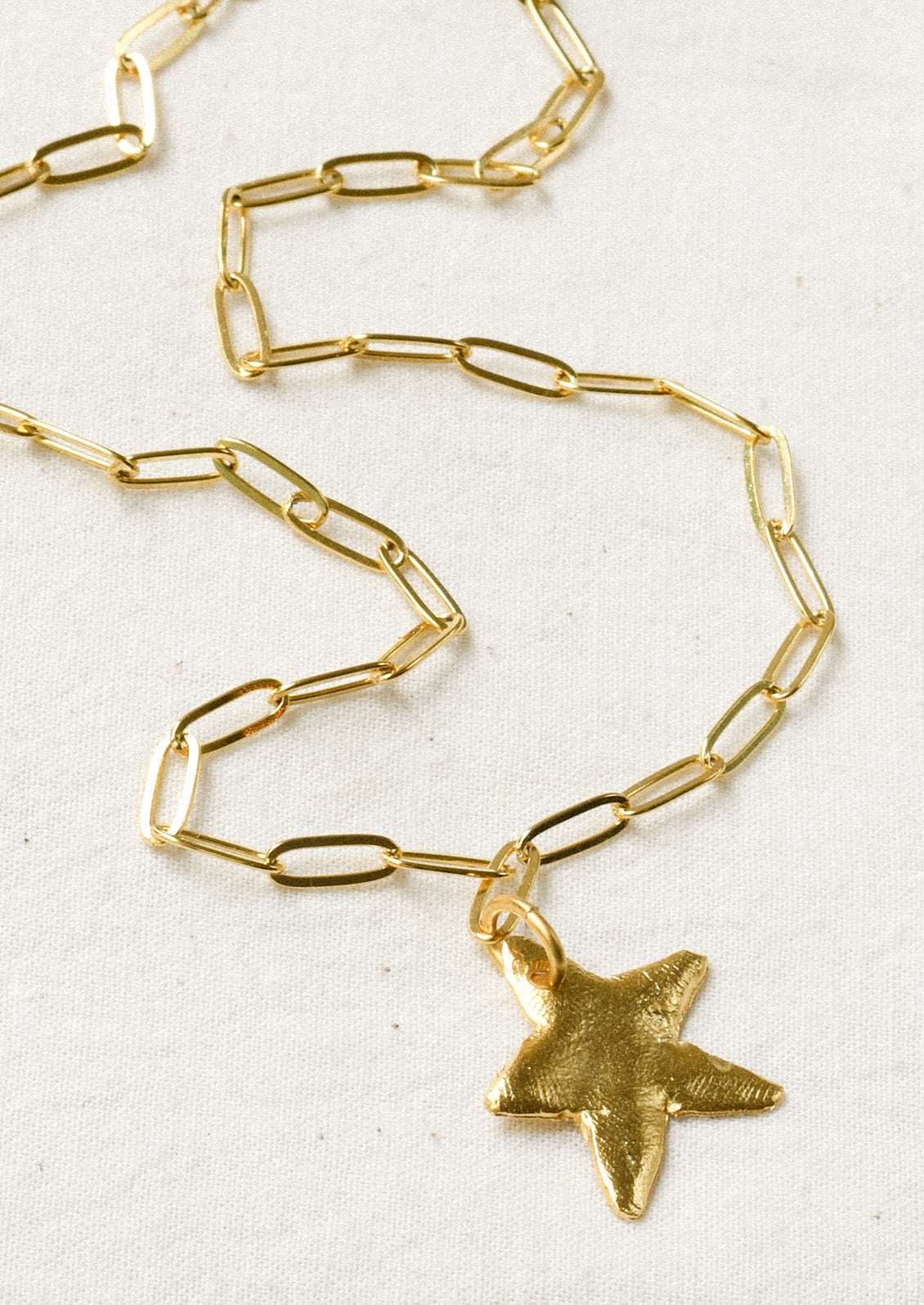 A gold paperclip chain necklace with a large star pendant.