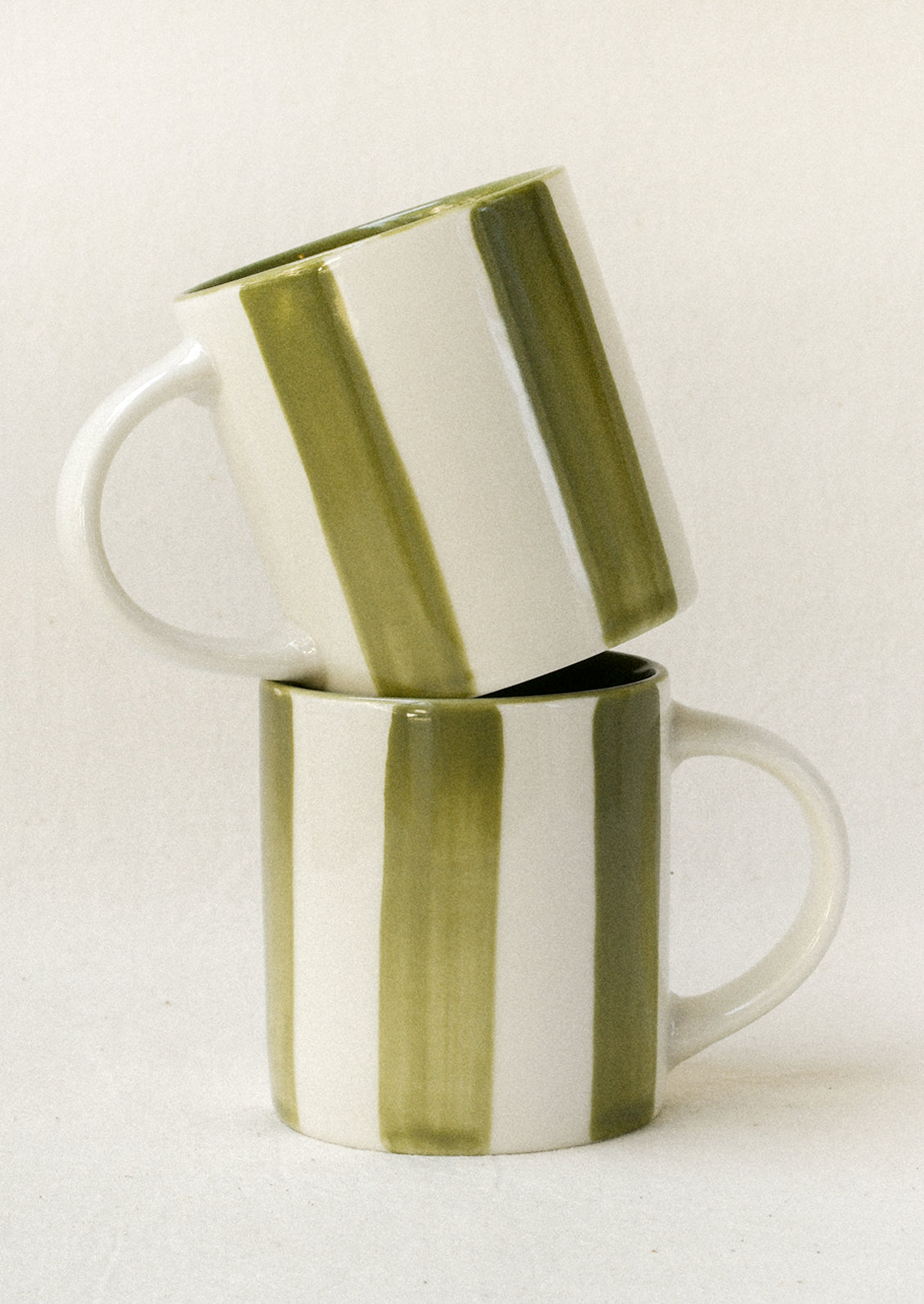 Small ceramic espresso cups with green stripes stacked on top of one another.