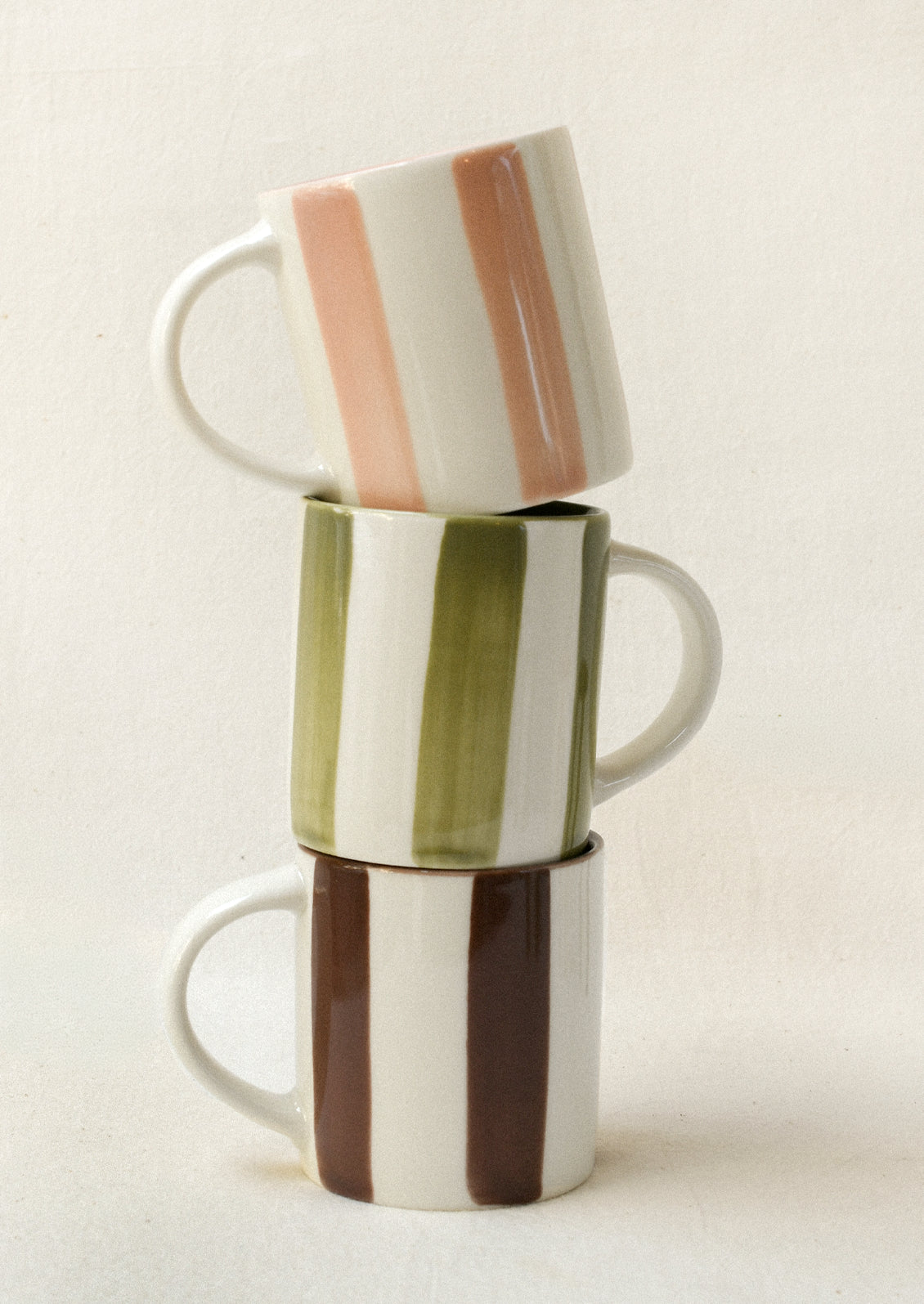 A stack of small ceramic espresso cups: one with pink stripes, one with green stripes, and one with brown stripes.