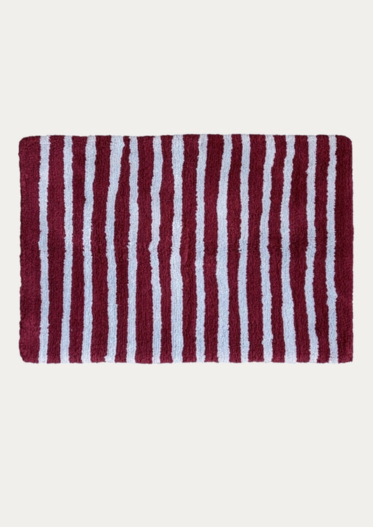 A rectangular bath rug with vertical burgundy and periwinkle stripes, shown flat against a light off-white background.