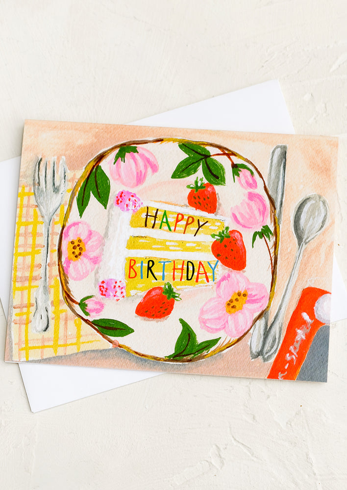 A birthday card with illustration of table setting with slice of cake on plate.