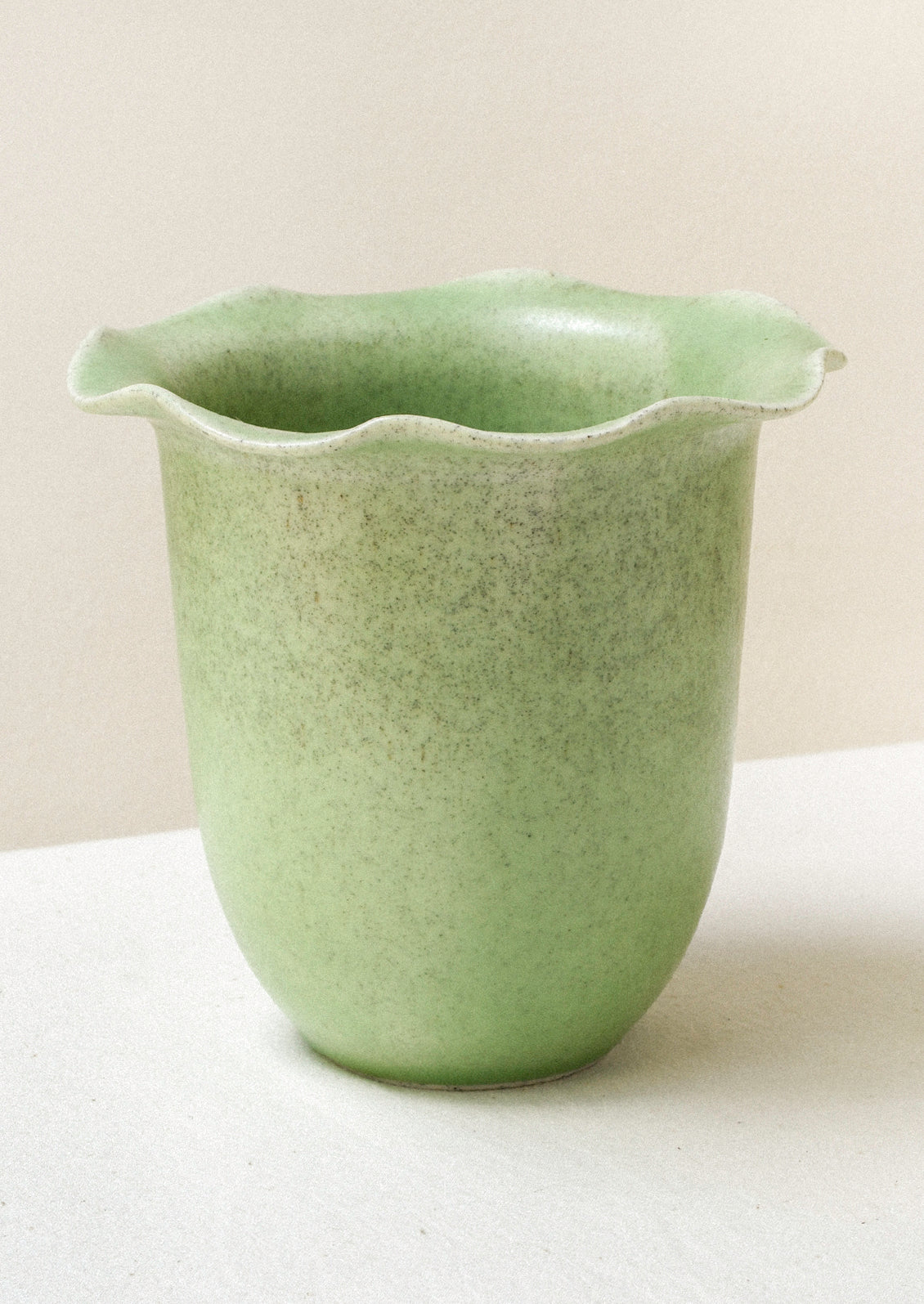A green ceramic speckled vase with a rippled lip design.