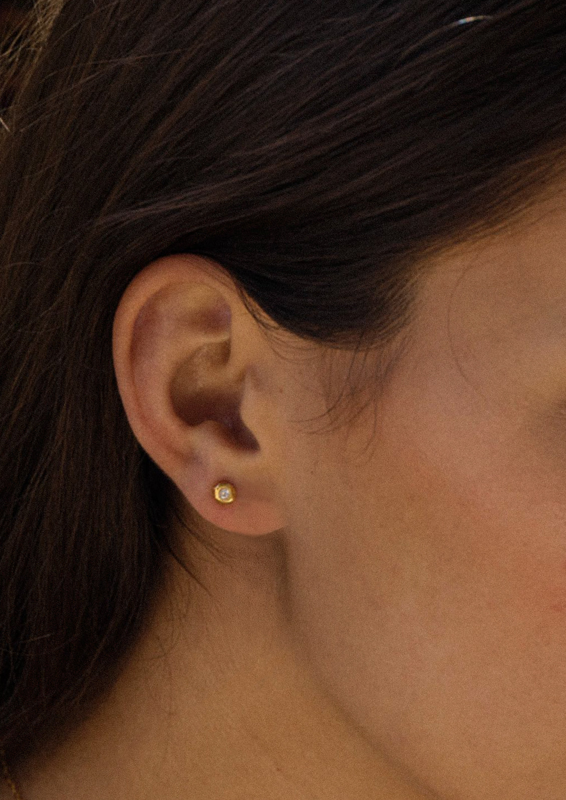 A woman wearing a gold stud earring with a crystal center.