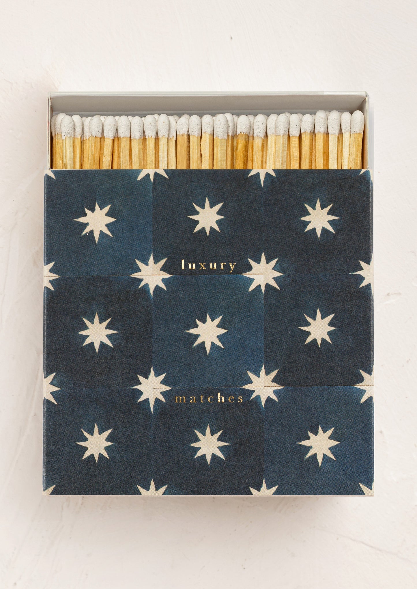A large square box of matches with navy and white star tile design on box, matches have white tips.