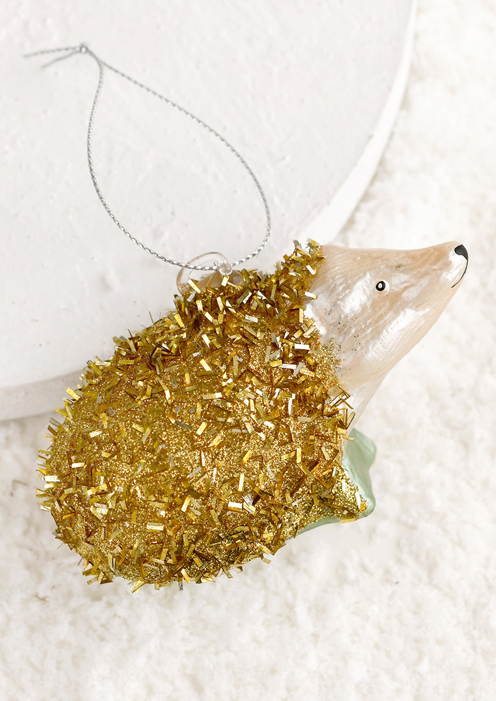 1: A holiday ornament of a hedgehog in gold tinsel.