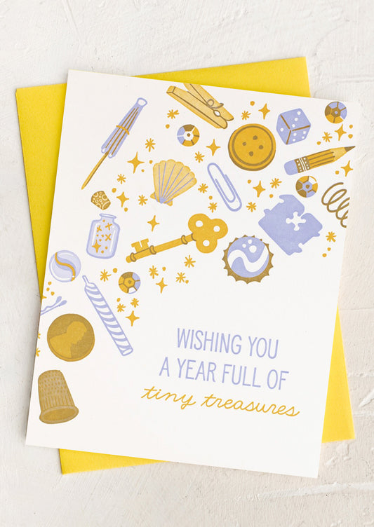 A greeting card with illustration of various charms and trinkets, text reads "Wishing you a year full of tiny treasures".