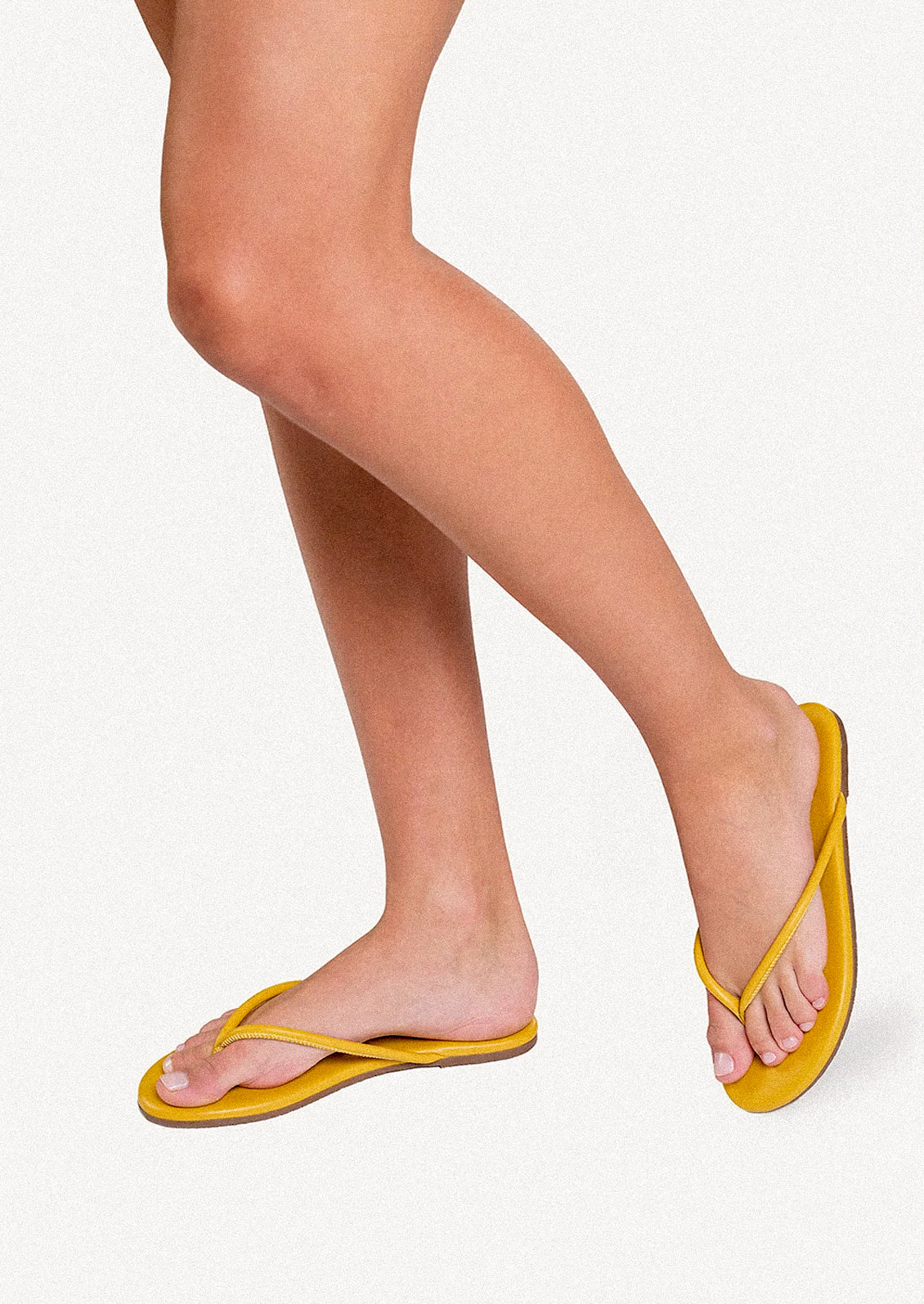 A person wearing a pair of leather TKEES sandals with a tubular strap design in deep yellow.