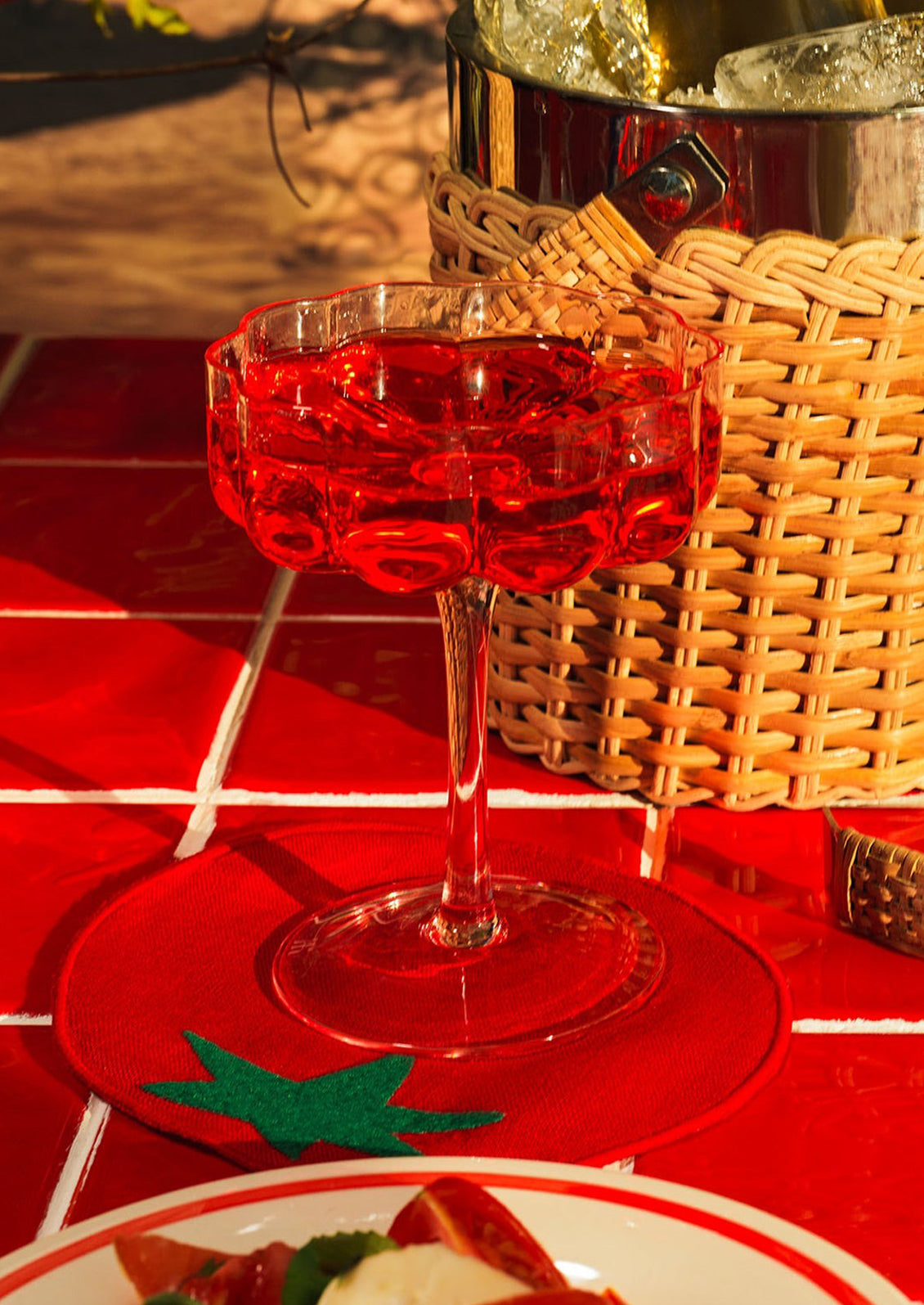 Red cocktail in a glass on a red checkered tablecloth with a wicker basket in the background.