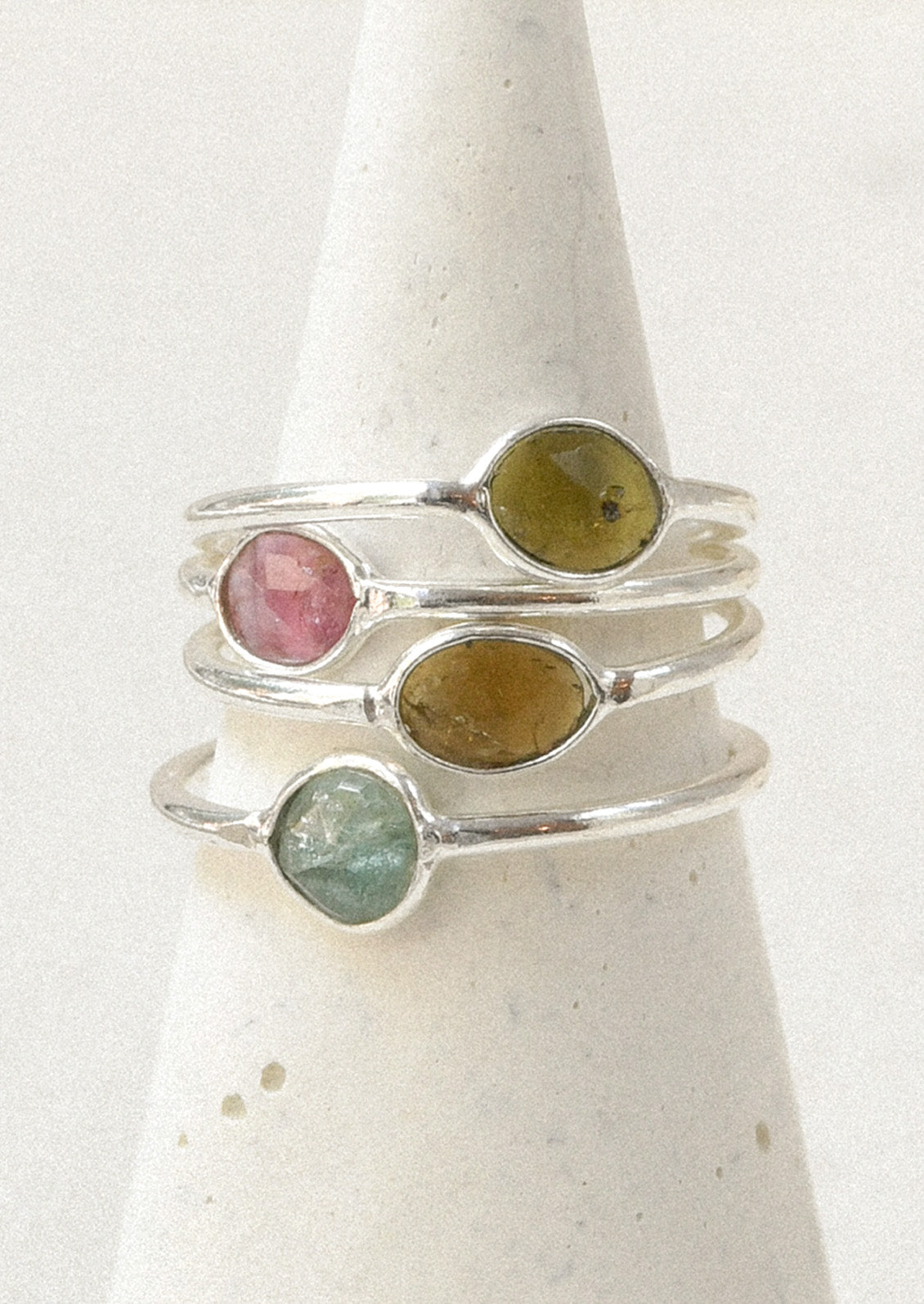 Four sterling silver rings stacked on top of one another with natural tourmaline stones in varying colors.