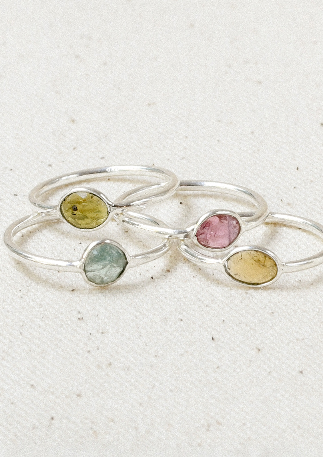 Four sterling silver rings stacked on top of one another with natural tourmaline stones in varying colors.