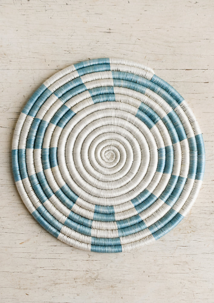 A woven sweetgrass trivet with geometric pattern in white and sky blue.