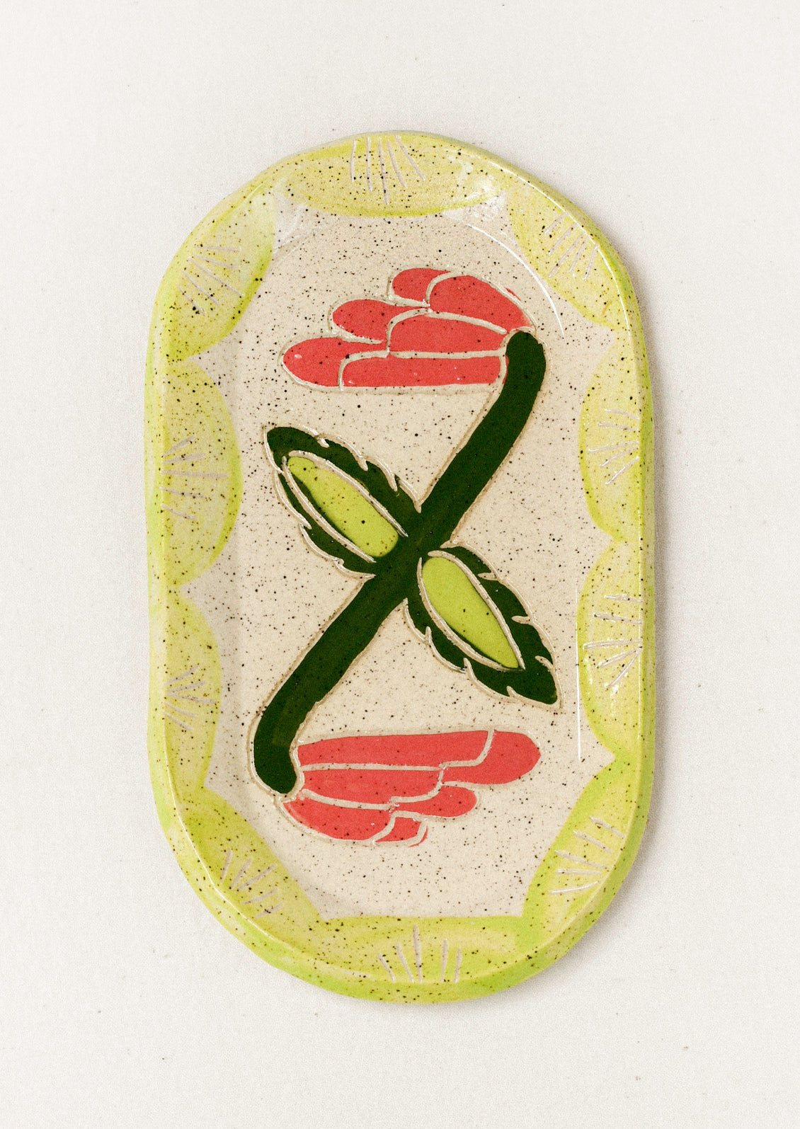 A ceramic oval catchall tray with an etched tulip flower in the center and a bright green painted scallop border.