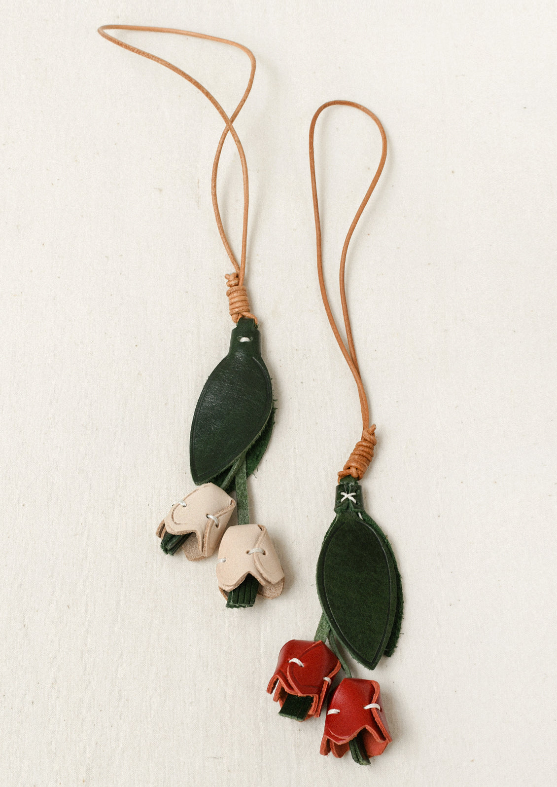 Two leather bag charms shaped like a tulip with red and cream petals and green leaves.