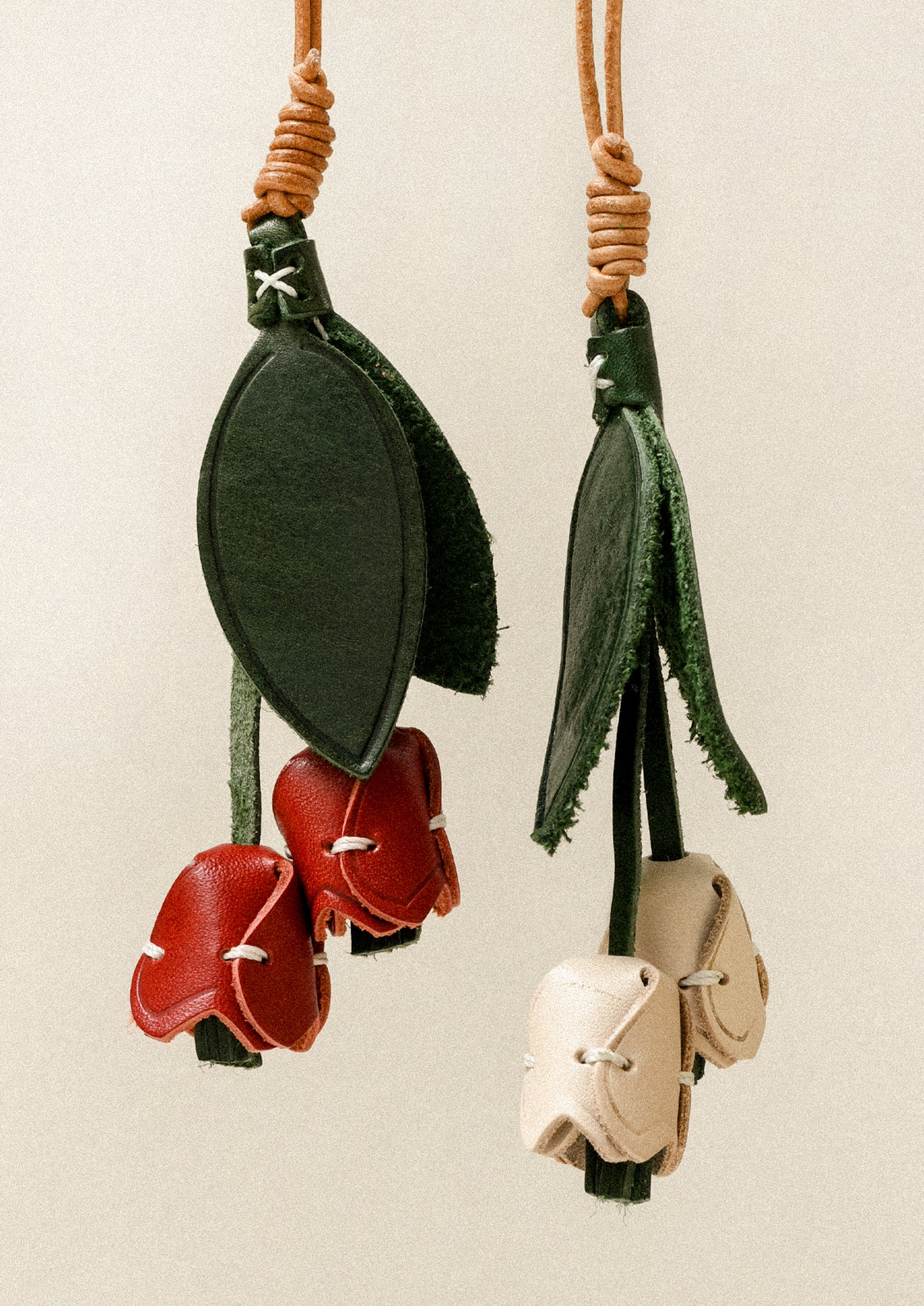Two leather bag charms shaped like a tulip with red and cream petals and green leaves.
