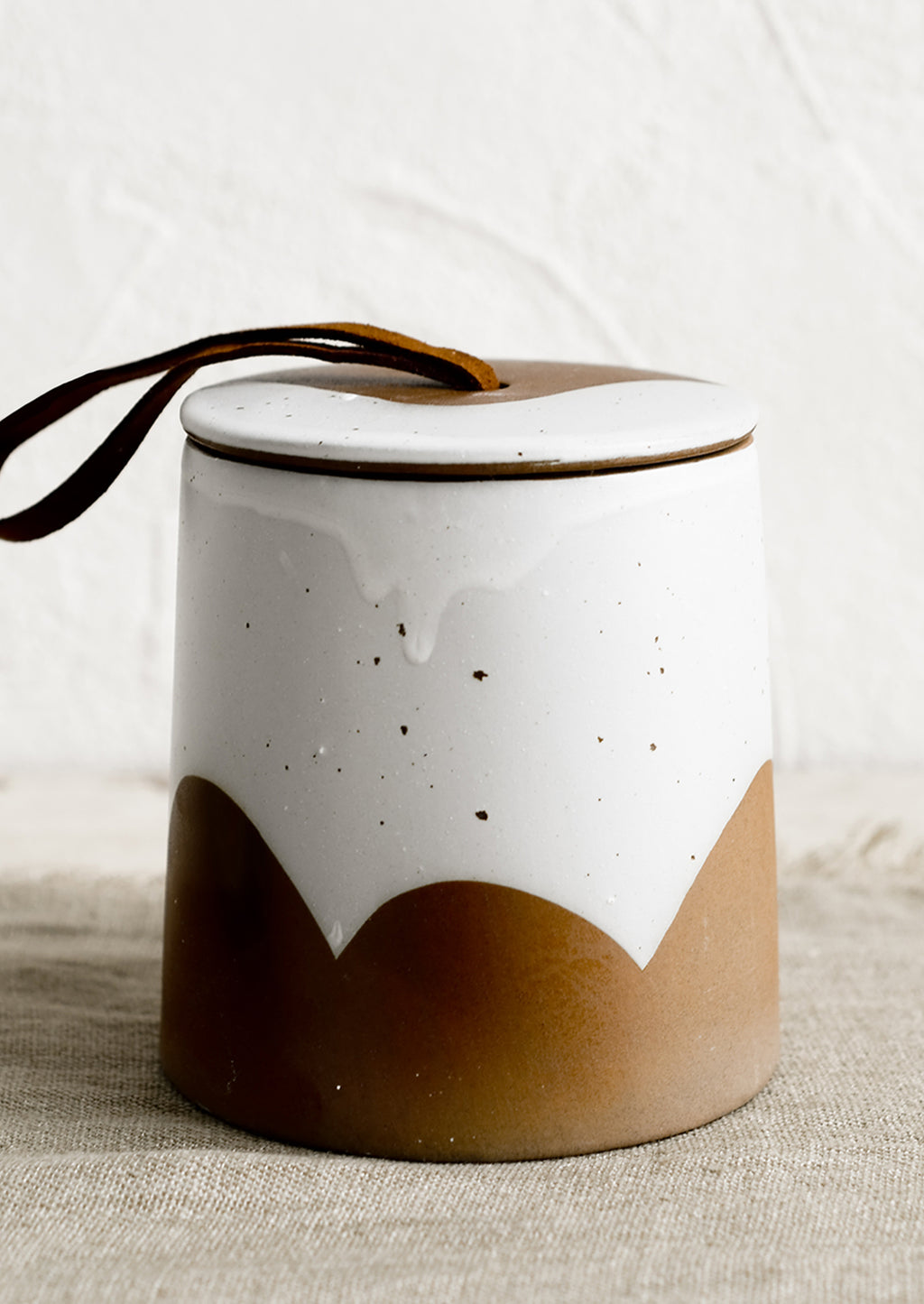 1: A brown and white ceramic storage jar with leather tie on lid.