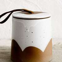 1: A brown and white ceramic storage jar with leather tie on lid.