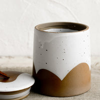2: A brown and white ceramic storage jar with leather tie on lid.