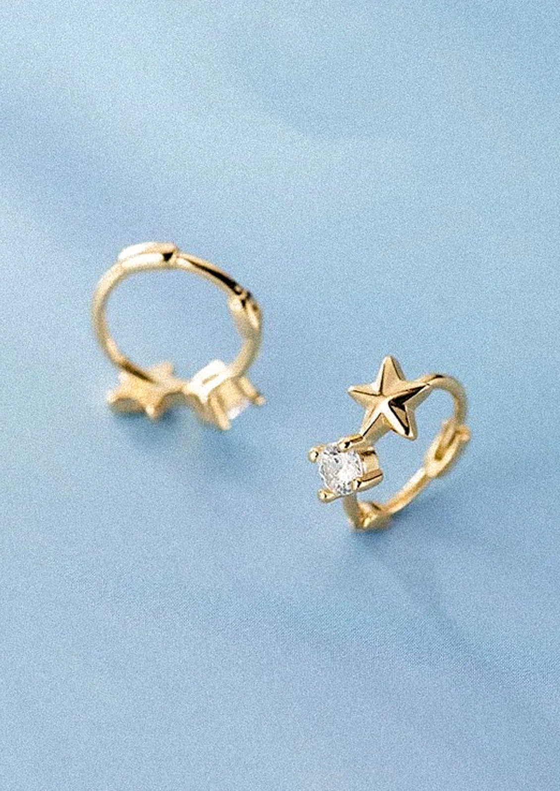 A pair of gold huggie hoop earrings with a star and a cubic zirconia gem on a blue background.