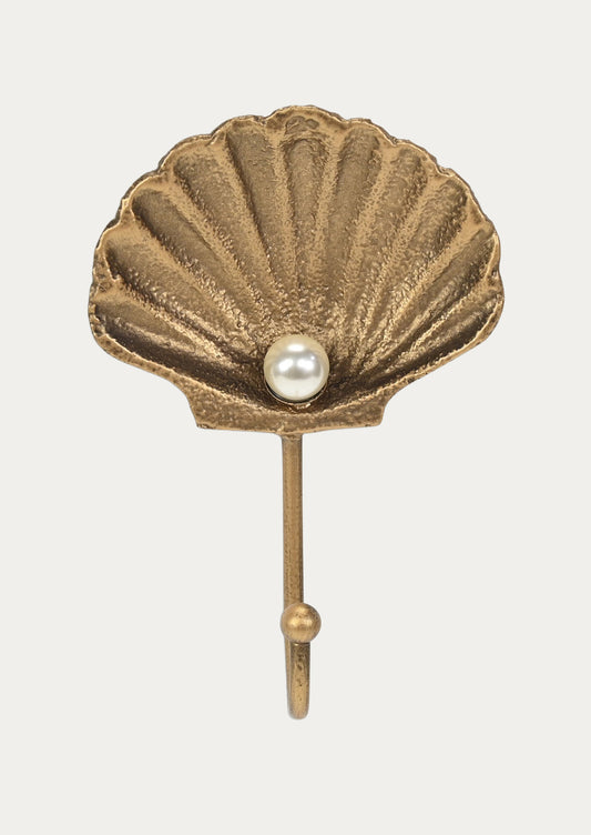 A handcrafted gold cast iron wall hook in the shape of a shell with a faux pearl in the center on a white background.