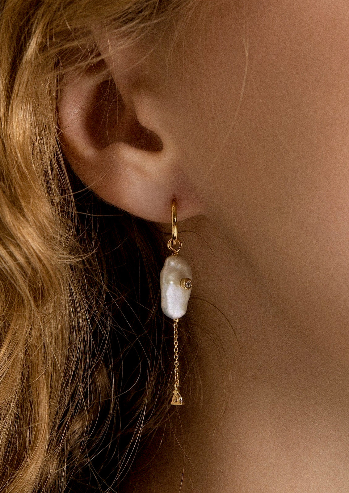 A dangling pearl earring hanging from a woman's ear.