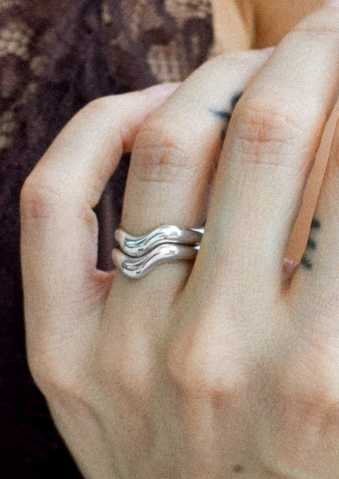 A woman wearing two sterling silver rings with a wavy design.
