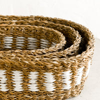2: An oval shaped storage basket in seagrass with woven white detail.
