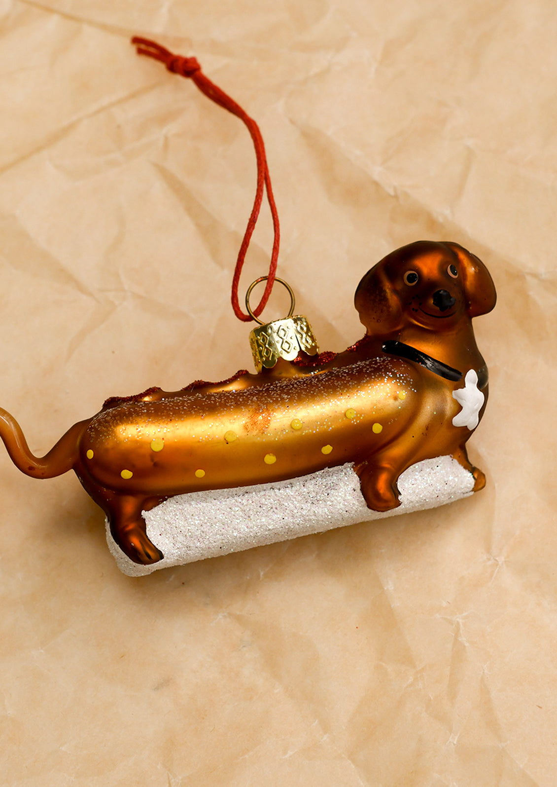 A glass ornament depicting a dachshund dog dressed as a hot dog.