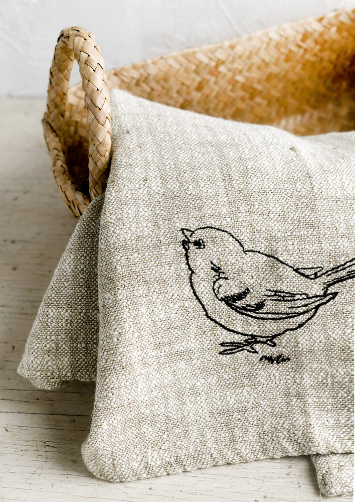 A natural linen tea towel embroidered with bird in black stitching.