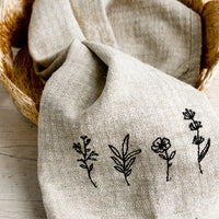 Flowers: A natural linen tea towel embroidered with flowers in black stitching.