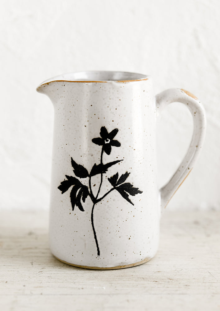 A small speckled white ceramic creamer pitcher with black flower silhouette.