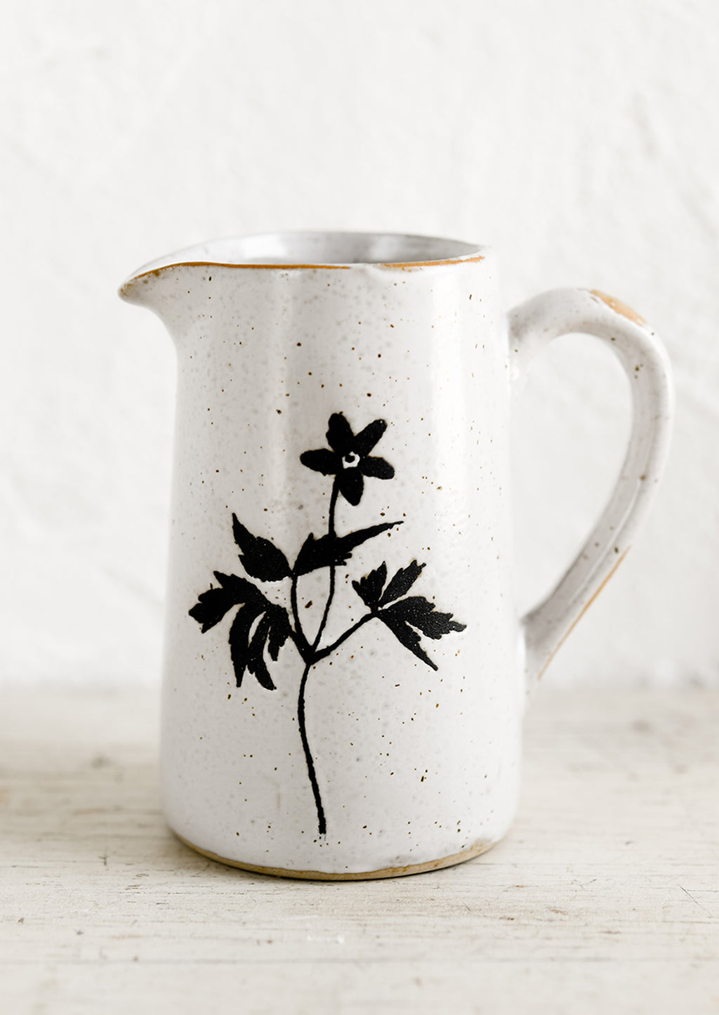 2: A small speckled white ceramic creamer pitcher with black flower silhouette.