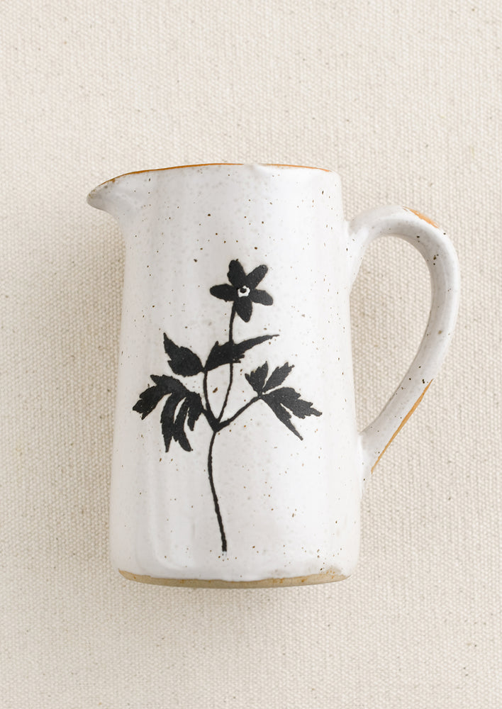 1: A small speckled white ceramic creamer pitcher with black flower silhouette.