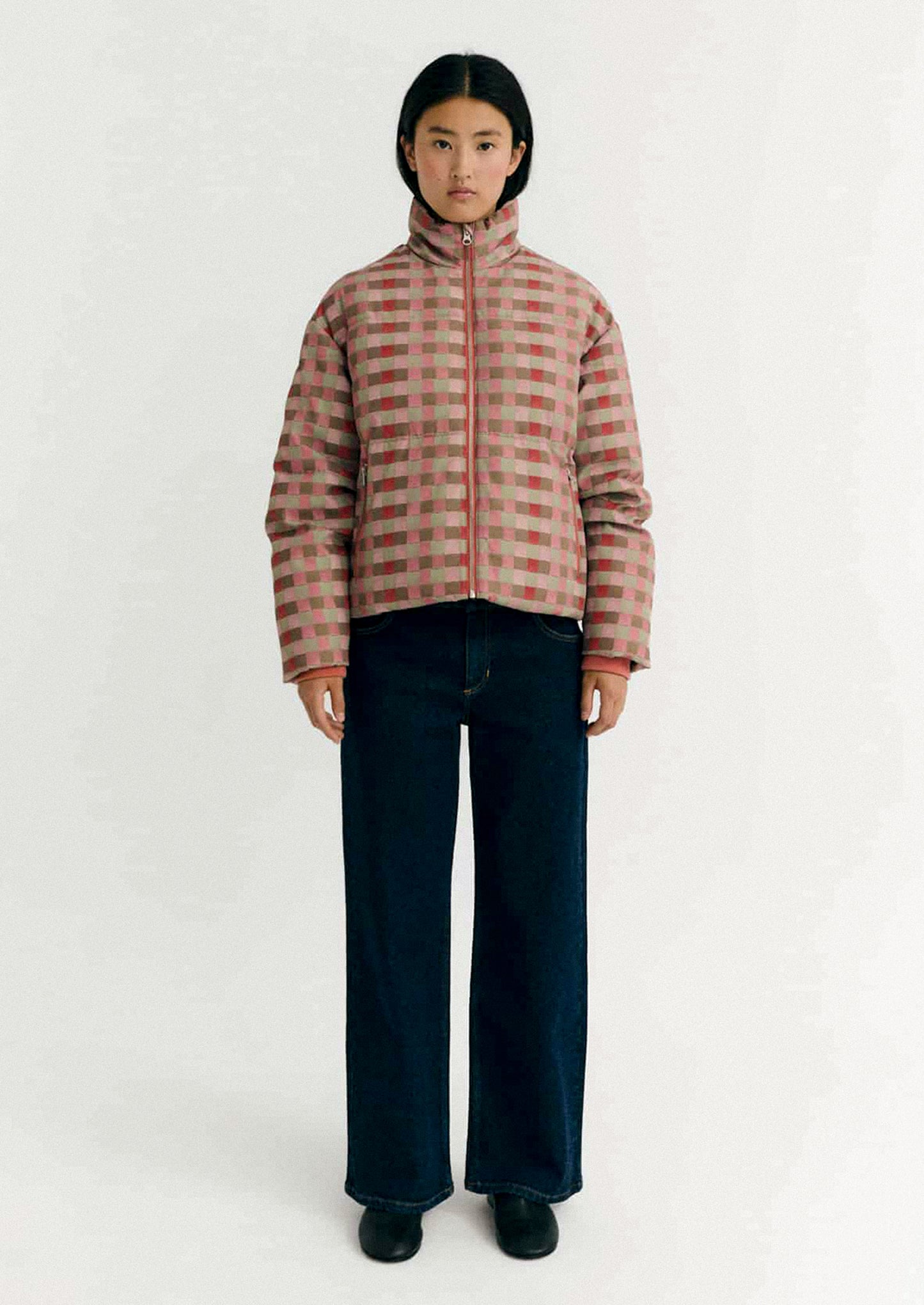 Person wearing a checkered puffer jacket on a white background.
