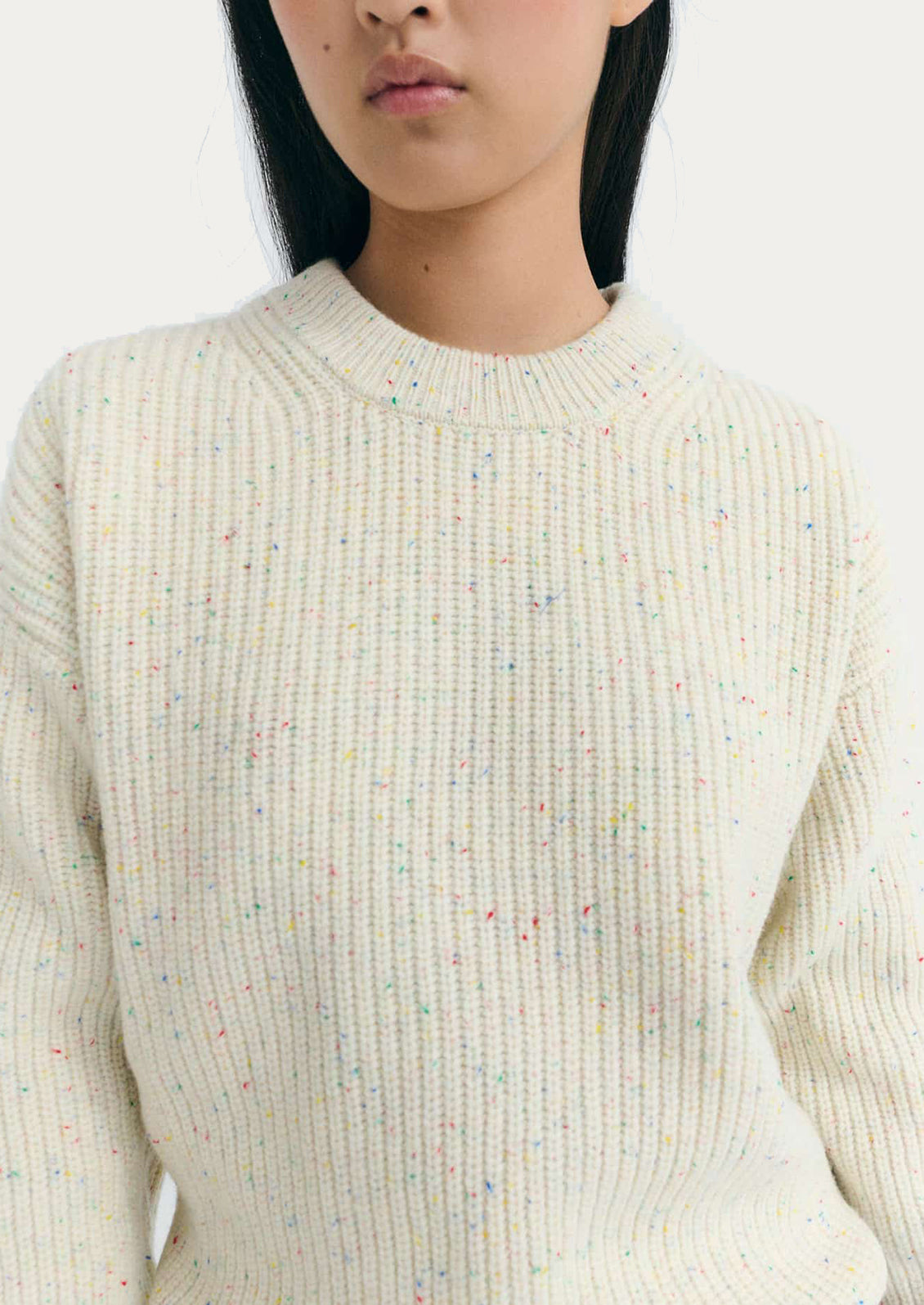 Person wearing a cream ribbed sweater with multicolored speckles.