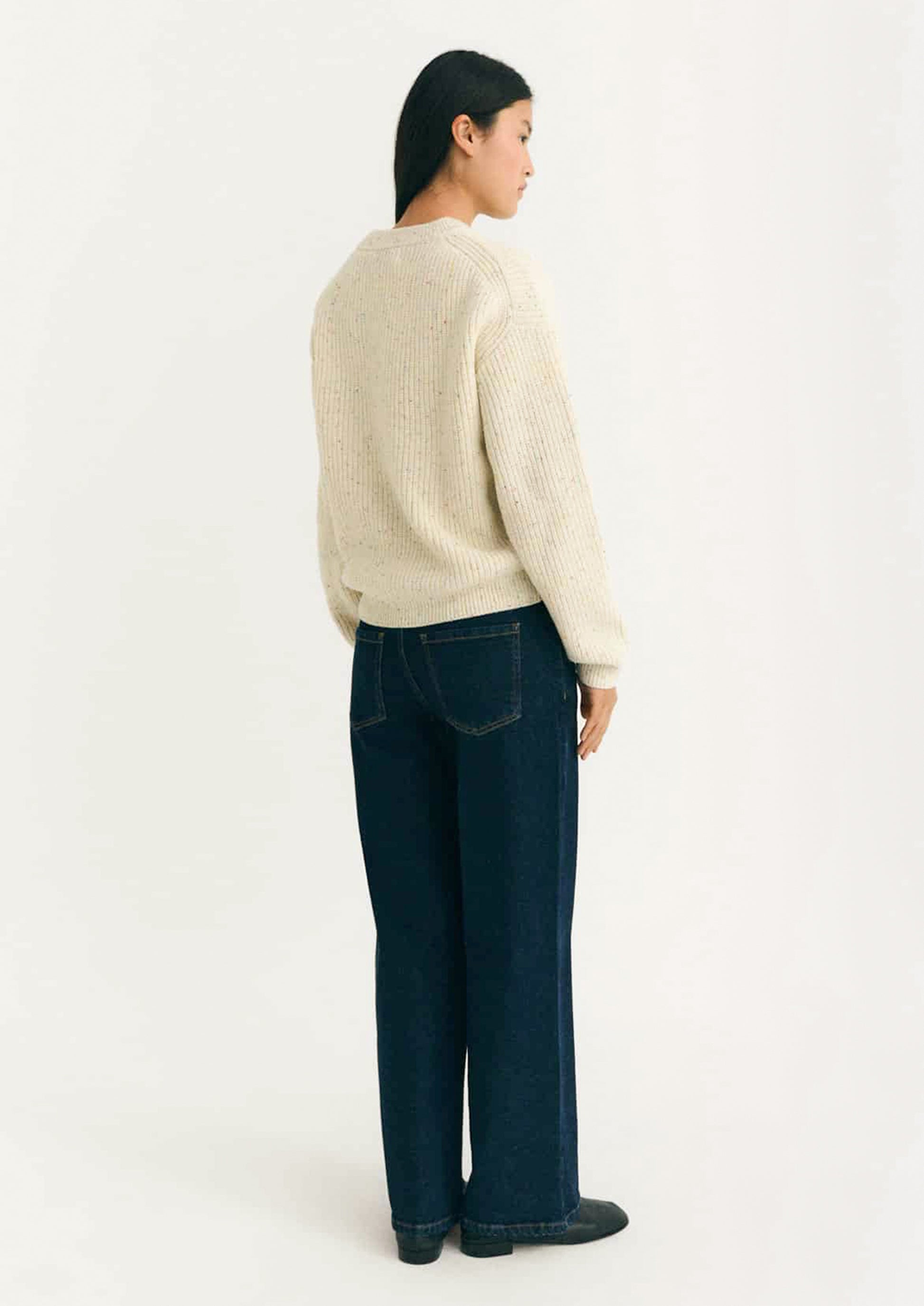 Person wearing a cream ribbed sweater with multicolored speckles.