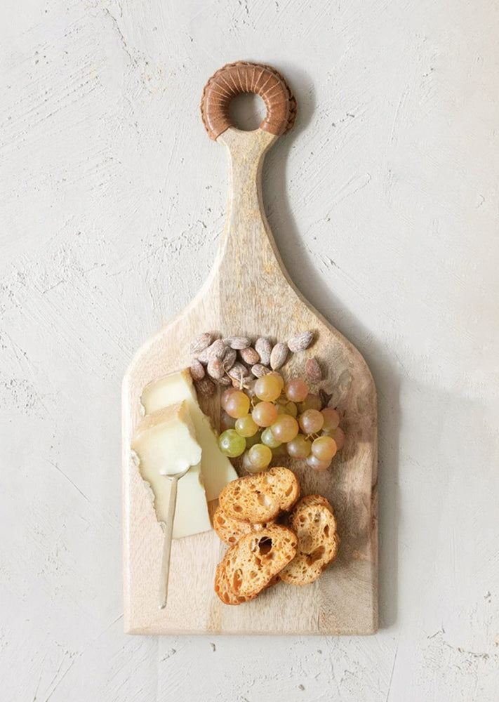 A wooden cutting board holding cheese, fruit and nuts.