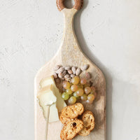2: A wooden cutting board holding cheese, fruit and nuts.