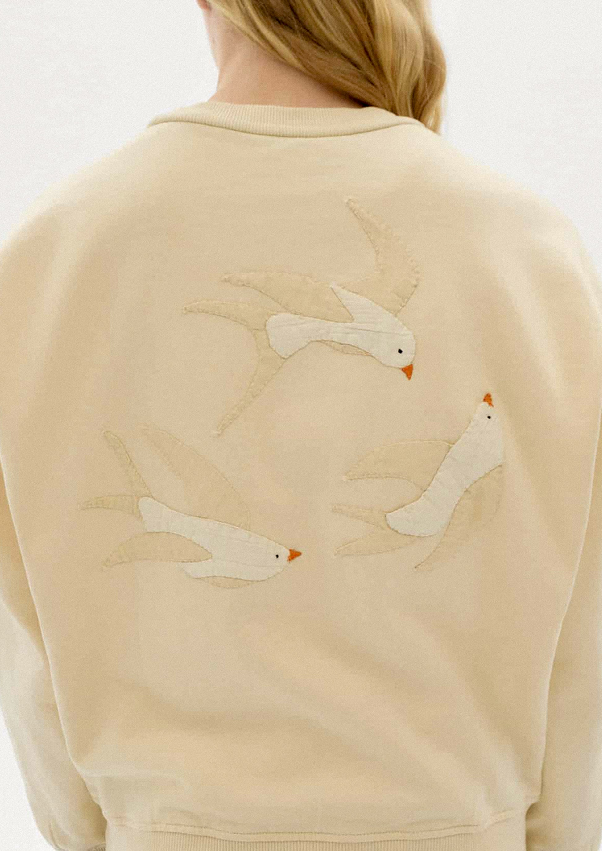 Beige sweatshirt with swallowtail bird applique detailing on back.