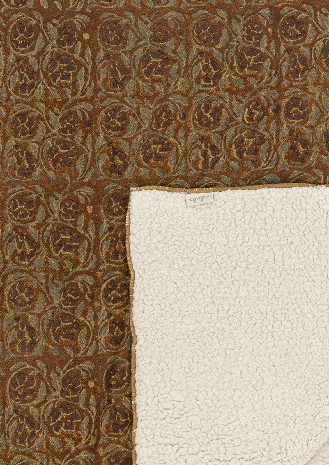 A close-up of a patterned blanket showing its brown and beige floral medallion design, with a folded corner revealing a thick, off-white sherpa or fleece backing.