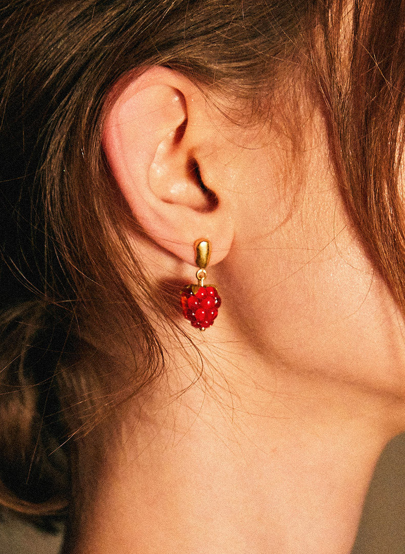 2: A person wearing a pair of glass earrings in shape of raspberries.