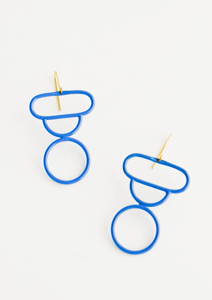 Bright blue enamel earrings in the shape of a circle, half circle, and oval stacked atop each other.