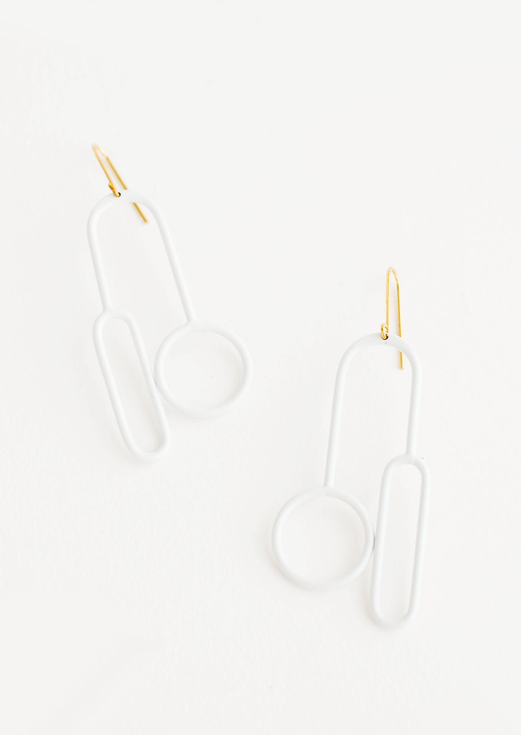 Blanco: Arced white earrings with one circle and one elongated oval at either end on a brass ear wire. 
