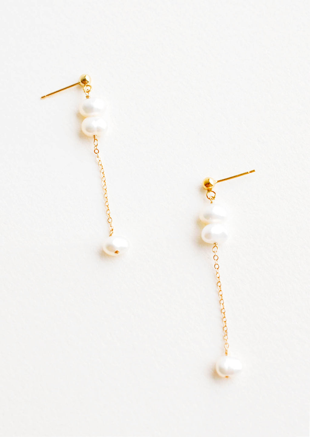 1: A pair of gold earrings with three pearls dangling from a post, and the third pearl is hanging from a fine gold chain.