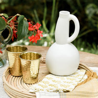 2: A table setting with ceramic pitcher and brass cups.
