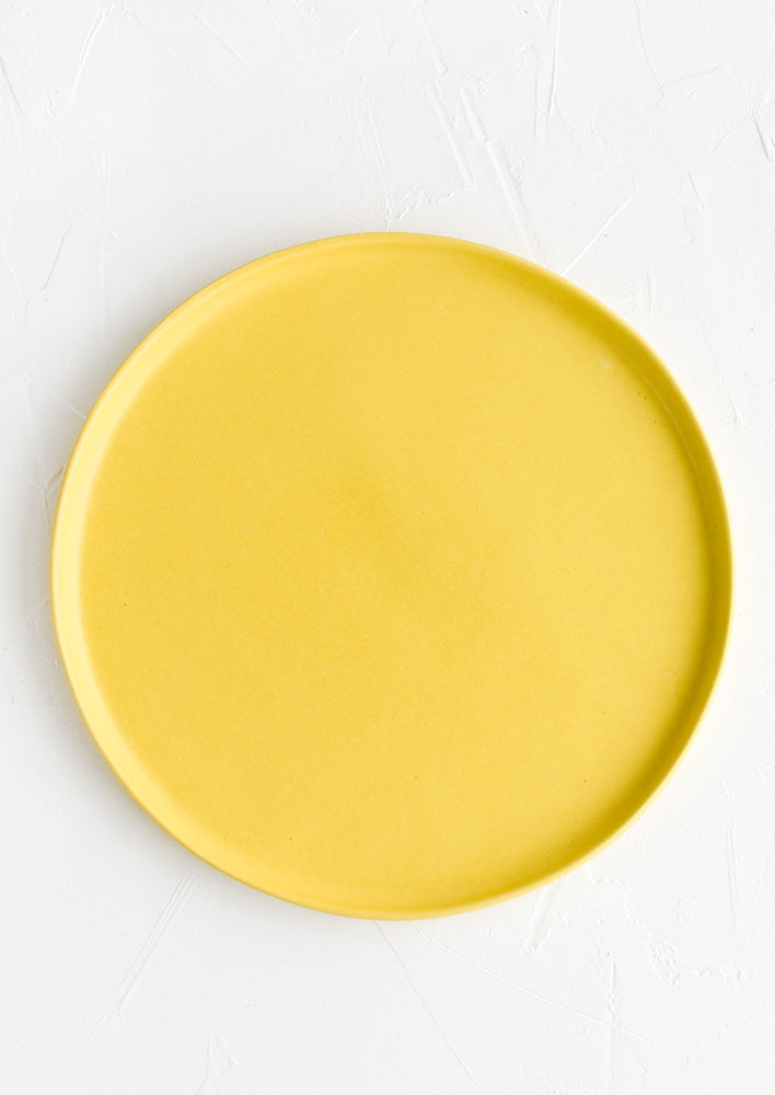 A round ceramic dinner plate in sun yellow.